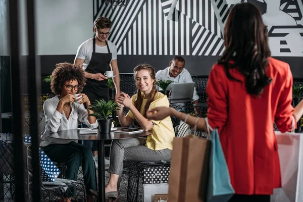 Junge Frau mit Einkaufstüten geht zu ihren Freunden in Café — Stockfoto