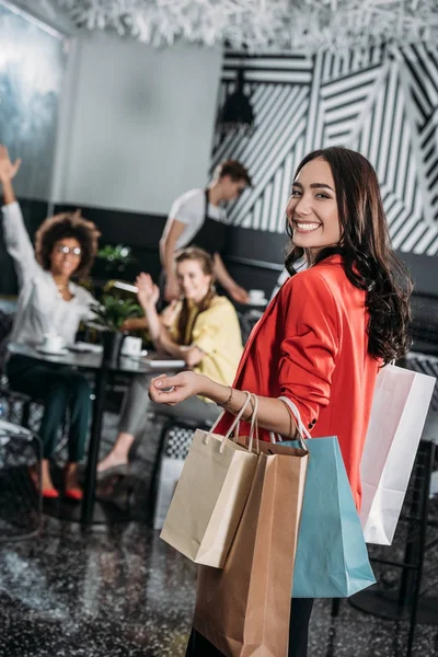 Mujer con bolsas de compras va a sus amigos en la cafetería - foto de stock