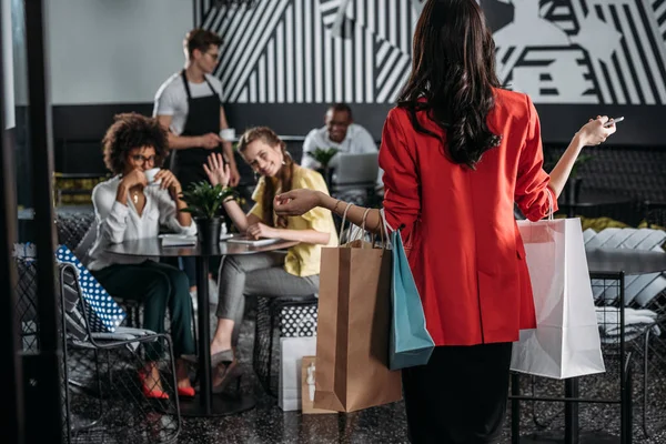 Mujer con bolsas de compras va a sus amigos en la cafetería - foto de stock