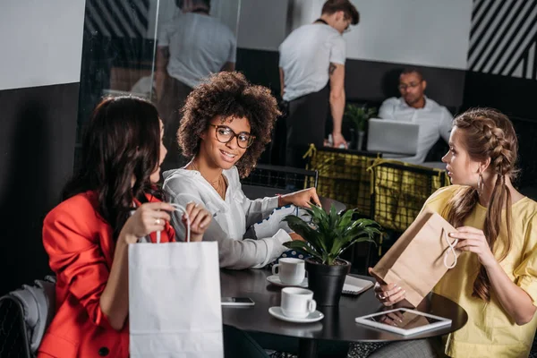 Grupo multiétnico de mujeres jóvenes con bolsas de compras en la cafetería — Stock Photo