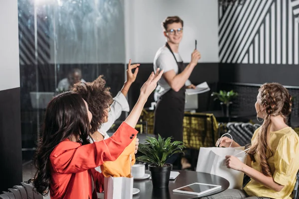 Group of stylish multiethnic women calling waiter in cafe — Stock Photo