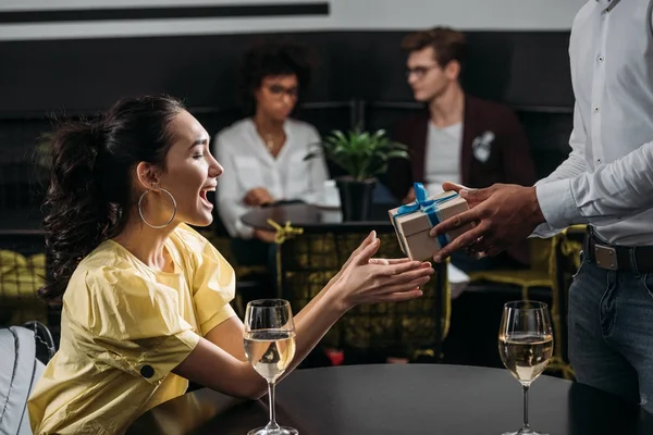 Happy emotional woman taking gift from boyfriend at restaurant — Stock Photo