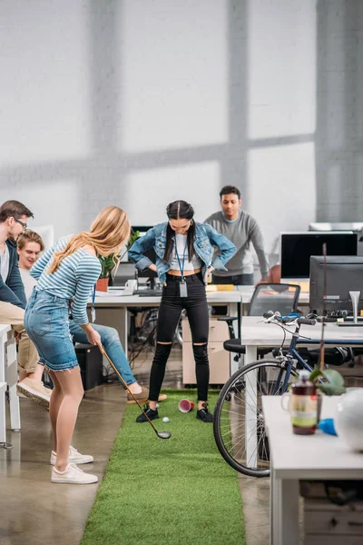 Compañeros alegres jugando en mini golf en la oficina moderna - foto de stock