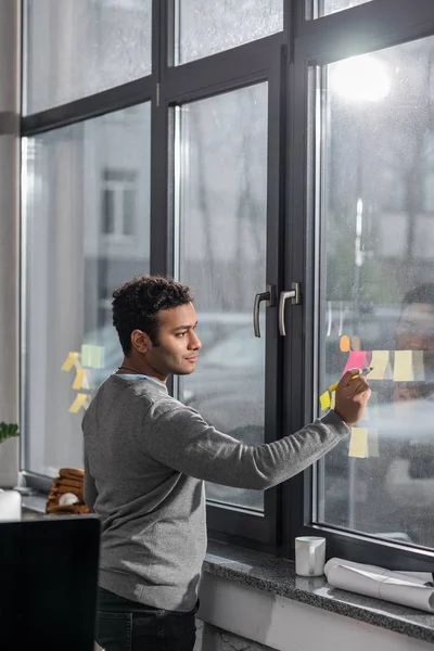 Jeune homme prenant des notes sur des autocollants à la fenêtre — Photo de stock