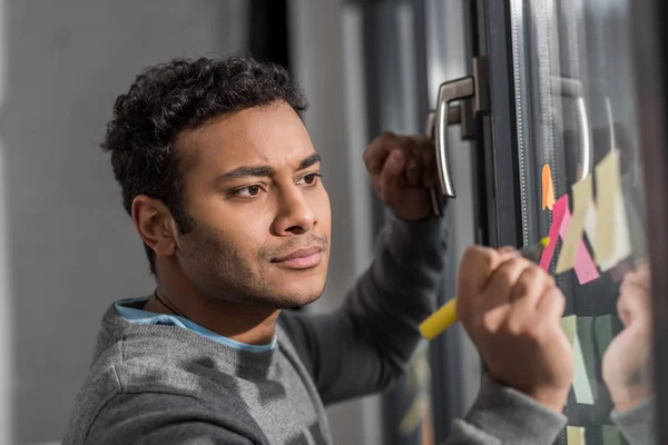 Junger Mann macht sich Notizen auf Aufkleber am Fenster — Stockfoto