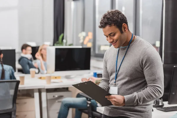 Glücklicher afrikanisch-amerikanischer Mann mit Namensschild, der im modernen Büro etwas auf Schrötlinge schreibt — Stockfoto