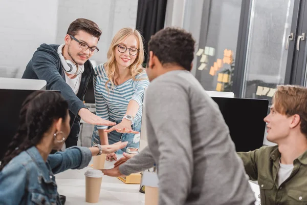 Cheerful multicultural business team making stack of hands at modern office — Stock Photo