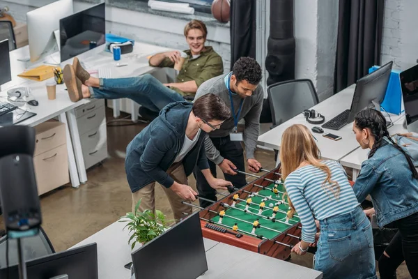 Багатонаціональні колеги грають у настільному футболі в сучасному офісі — стокове фото