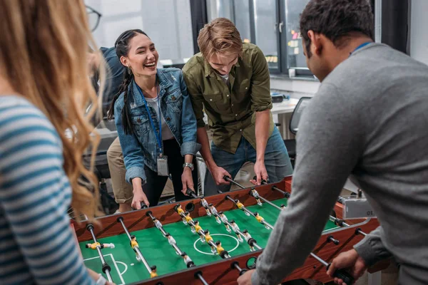 Gente multicultural feliz jugando en el futbolín en la oficina moderna - foto de stock