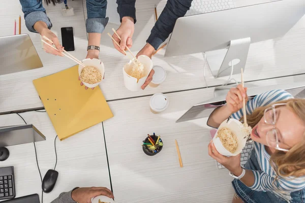 Vista dall'alto delle mani ritagliate con cibo tailandese sul tavolo da lavoro in un ufficio moderno — Foto stock