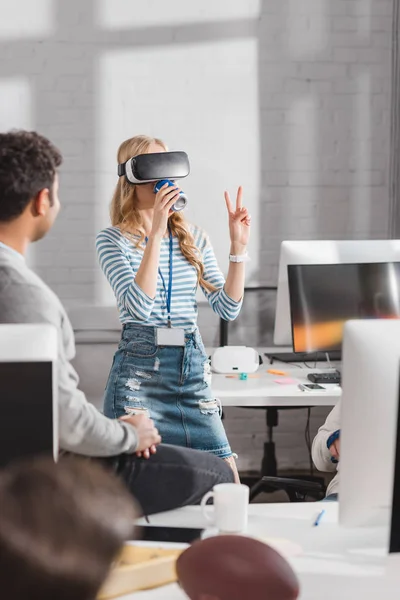 Young woman drinking beverage in virtual reality glasses at modern office — Stock Photo