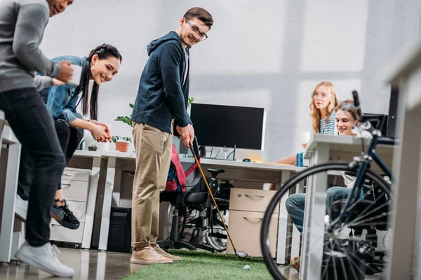 Рабочие веселятся в офисе, мужчина играет в мини-гольф — стоковое фото