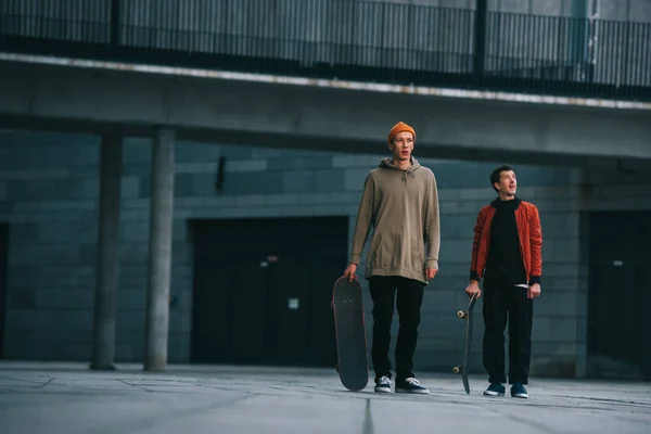 Jeunes hommes en tenue streetwear debout avec planches à roulettes — Photo de stock