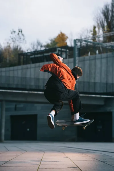 Skatista em casaco vermelho realizando truque de salto em localização urbana — Fotografia de Stock
