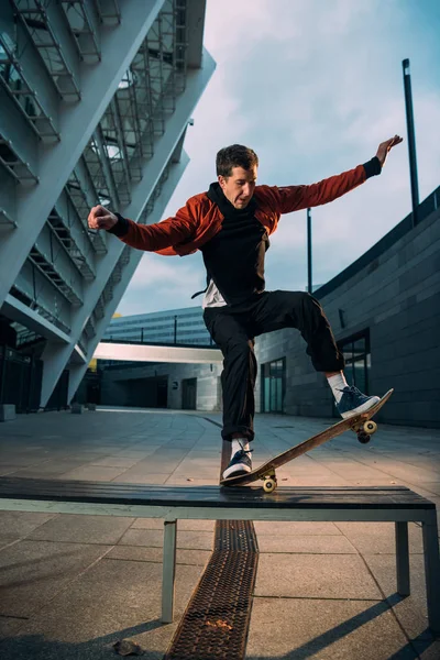 Young skateboarder in stylish outfit balancing with board on bench — Stock Photo