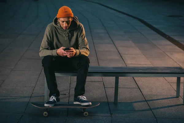 Skateboarder sitzt auf Bank und nutzt Smartphone — Stockfoto