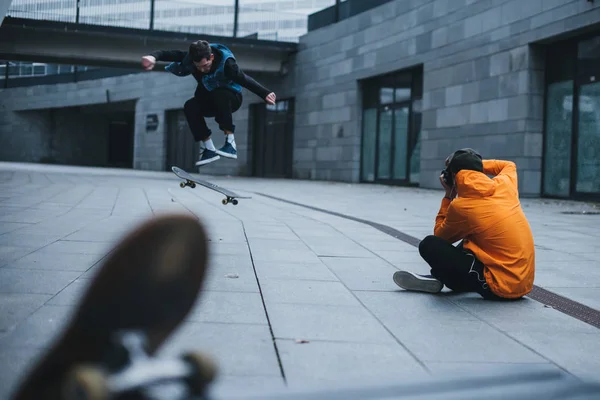 Hombre sentado en el suelo y tomar una foto de skate haciendo truco - foto de stock