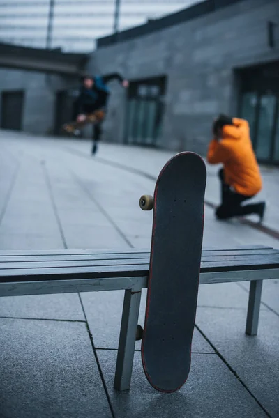 Skateboarder scattare foto di trucchi con skateboard appoggiato alla panchina in primo piano — Foto stock