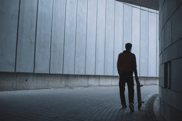 Skateboarder in piedi con tavola davanti al muro di cemento grigio — Foto stock