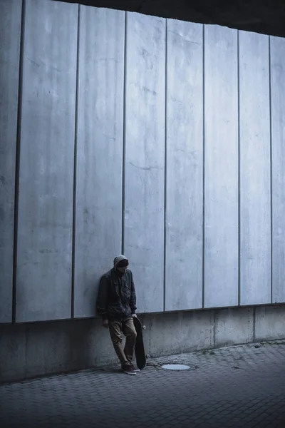 Скейтбордист з дошкою спирається назад на сіру бетонну стіну — стокове фото