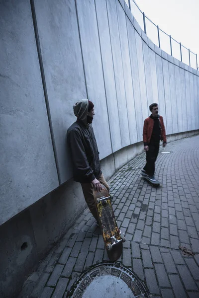 Jóvenes patinadores profesionales en atuendo callejero que pasan tiempo en el paisaje urbano - foto de stock