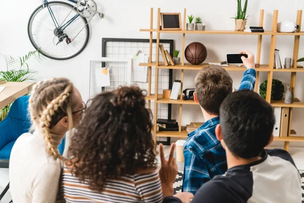 Vista posteriore di adolescenti multietnici seduti sul divano e scattare selfie con smartphone — Foto stock