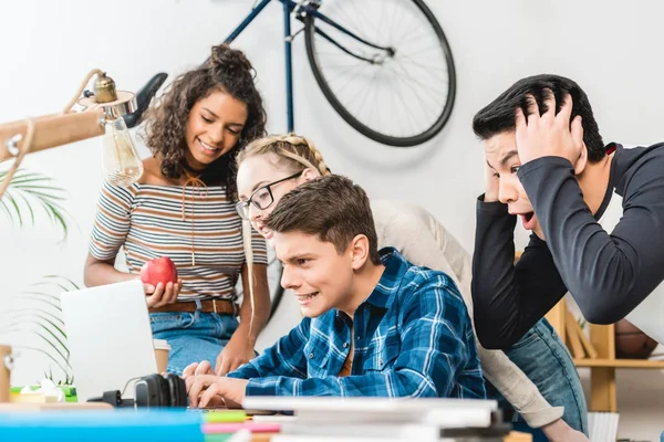 Gruppo di adolescenti multiculturali che guardano il computer portatile a tavola — Foto stock