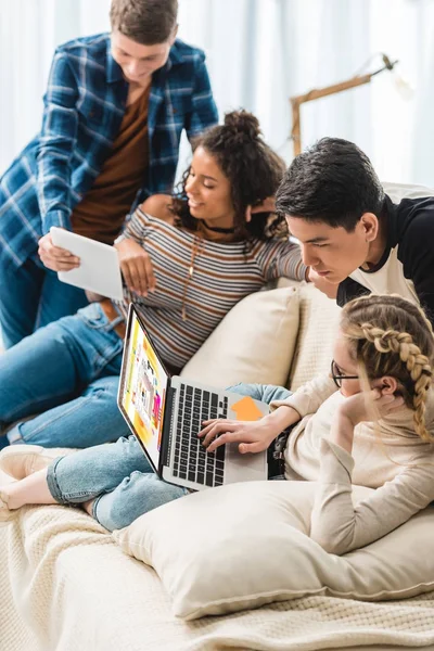 Smiling multicultural teenagers looking at laptop with loaded website — Stock Photo