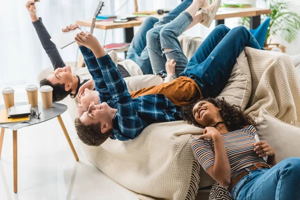 Adolescentes acostados en el sofá y tomando selfie con la tableta y el teléfono inteligente - foto de stock