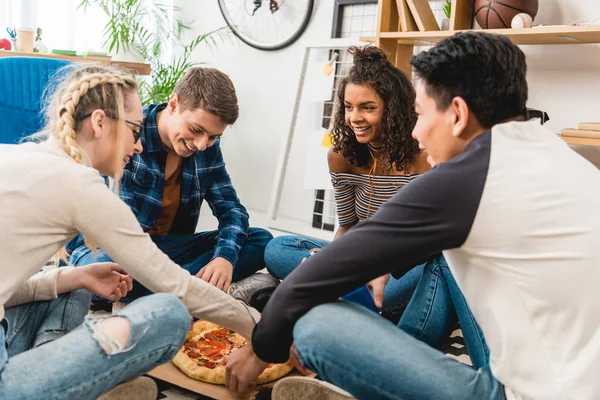 Amigos adolescentes multiétnicos sentados en el suelo y comiendo pizza - foto de stock