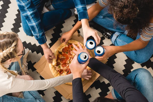 Cropped image of teens clinking with cans and taking pizza — Stock Photo