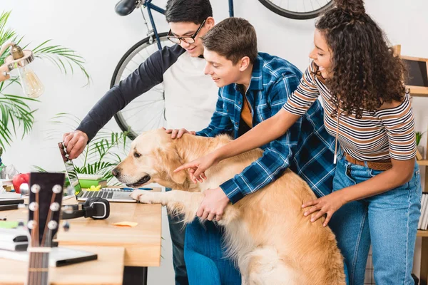 Adolescenti multietnici che mostrano qualcosa sul computer portatile al cane — Foto stock