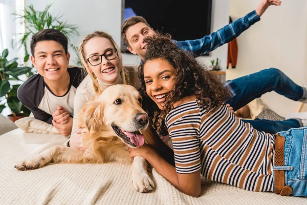 Happy multiethnic teenagers palming dog and looking at camera — Stock Photo