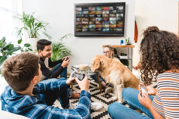 Grupo de cuatro adolescentes multiétnicos jugando videojuegos en casa - foto de stock