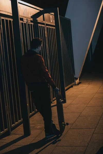 Uomo in piedi con skateboard all'aperto a tarda notte — Foto stock