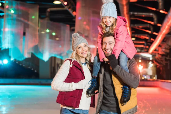 Felice giovane famiglia sorridente alla macchina fotografica, mentre trascorrere del tempo insieme sulla pista di pattinaggio — Foto stock