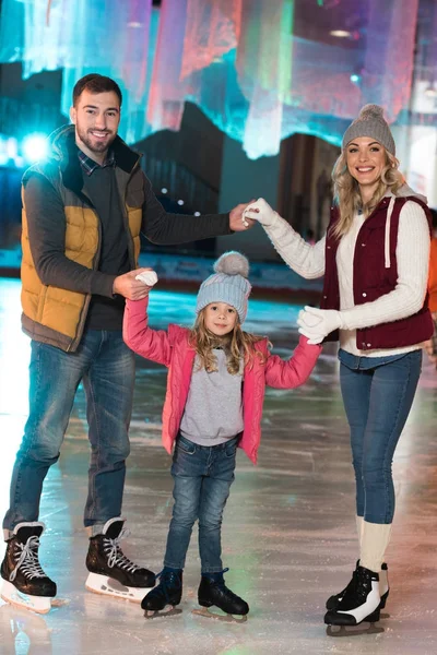 Heureux jeune famille tenant la main et souriant à la caméra sur patinoire — Photo de stock