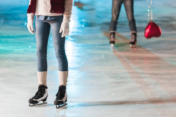 Cropped shot of young woman standing on rink while boyfriend with heart shaped balloon standing behind — Stock Photo