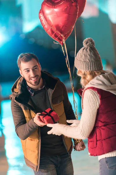 Glücklicher junger Mann überreicht Freundin am Valentinstag Geschenkbox auf Eisbahn — Stockfoto