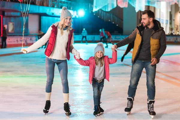 Heureux jeune famille tenant la main et souriant à la caméra sur patinoire — Photo de stock