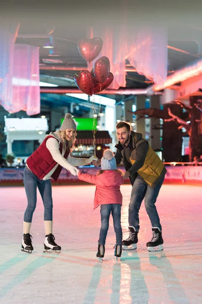 Happy family with one child holding heart shaped balloons on skating rink — Stock Photo
