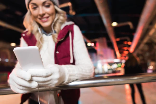 Close-up view of smiling young woman in earphones using smartphone while standing on rink — Stock Photo