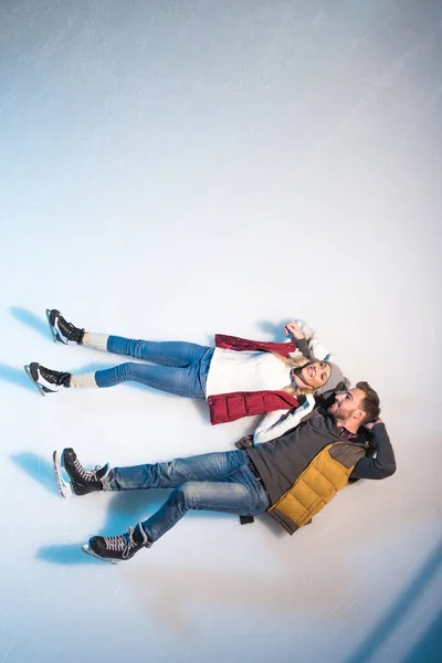 Vista superior de belo feliz jovem casal deitado juntos no gelo da pista de patinação — Fotografia de Stock