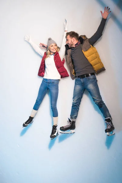 Hermosa feliz joven pareja acostados juntos en el hielo de pista de patinaje - foto de stock