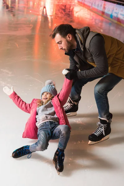 Father holding hand of cute little daughter falling on rink — Stock Photo