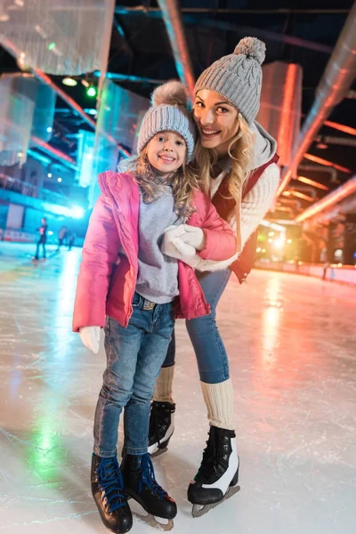 Beautiful happy mother and daughter smiling at camera while standing together on skating rink — Stock Photo