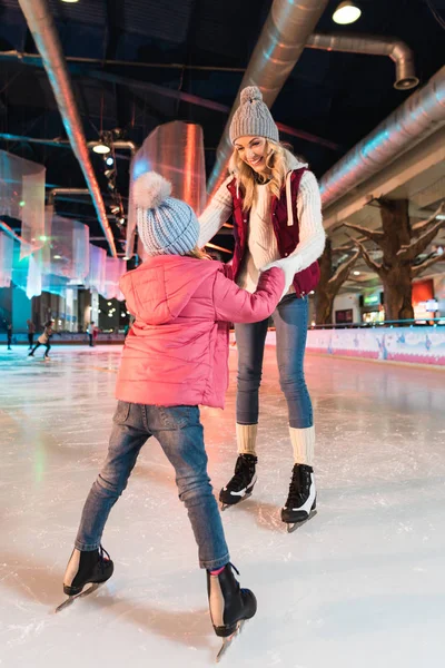 Happy mother and daughter holding hands and looking at each other on skating rink — Stock Photo