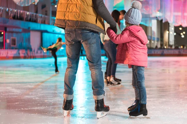 Recortado disparo de padre e hija tomados de la mano mientras están de pie juntos en pista de patinaje - foto de stock