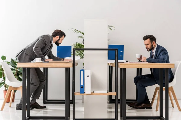 Vista lateral de los empresarios que trabajan y beben café en el lugar de trabajo - foto de stock