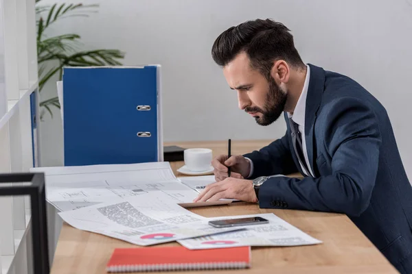 Geschäftsmann sitzt am Tisch, schaut sich Dokumente an und schreibt etwas — Stockfoto